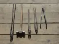 Ensemble d'outils de maréchal-ferrant : pinces, marteau et autres instruments sur fond de bois.