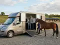 Un homme et une femme chargent un cheval dans un **dimension van chevaux 2 places** sur un terrain d'équitation.