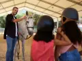 Un instructeur d'équitation souriant caresse un cheval blanc. Deux enfants, casqués, regardent.