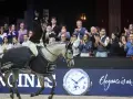 Cavalier(e) saluant la foule, son cheval gris couvert d'une cape aux couleurs de la Longines FEI Jumping World Cup.