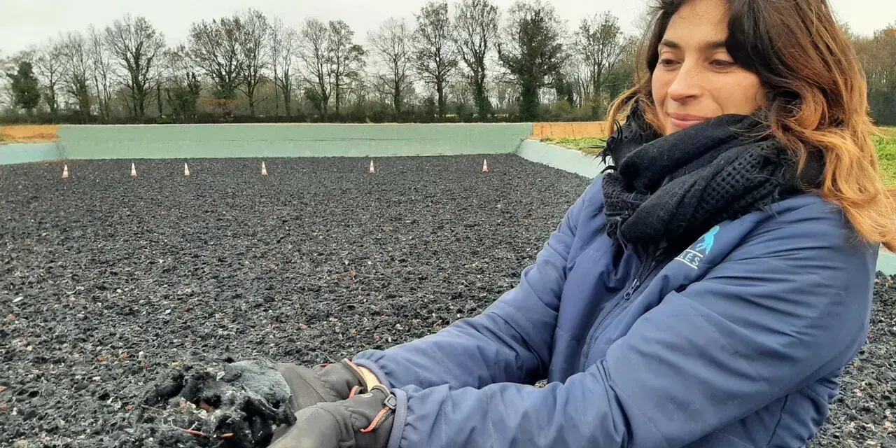 Une femme tient dans ses mains un échantillon de fibre, un avis carrière en fibre. L'arrière-plan montre une carrière équestre.