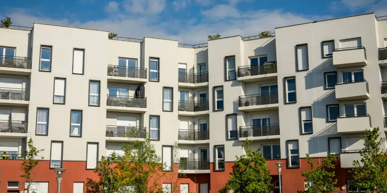 Immeuble moderne aux balcons noirs, un **idéal de la loge** avec ses façades blanches et sa base rouge. Ciel bleu et nuages.