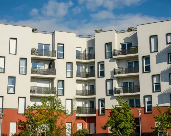 Immeuble moderne aux balcons noirs, un **idéal de la loge** avec ses façades blanches et sa base rouge. Ciel bleu et nuages.