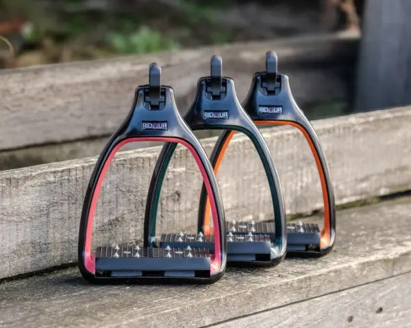 Trois étriers Rid'Up colorés (rose, vert, orange) sur un banc en bois. Avis positifs pour ces étriers.