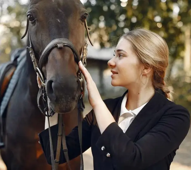 Une jeune femme caresse la tête d'un cheval noir, prête pour une séance de dressage équestre.