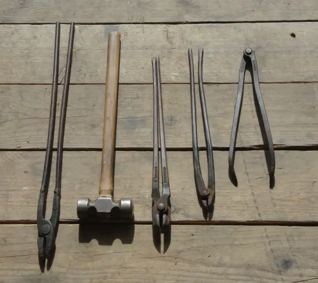 Ensemble d'outils de maréchal-ferrant : pinces, marteau et autres instruments sur fond de bois.
