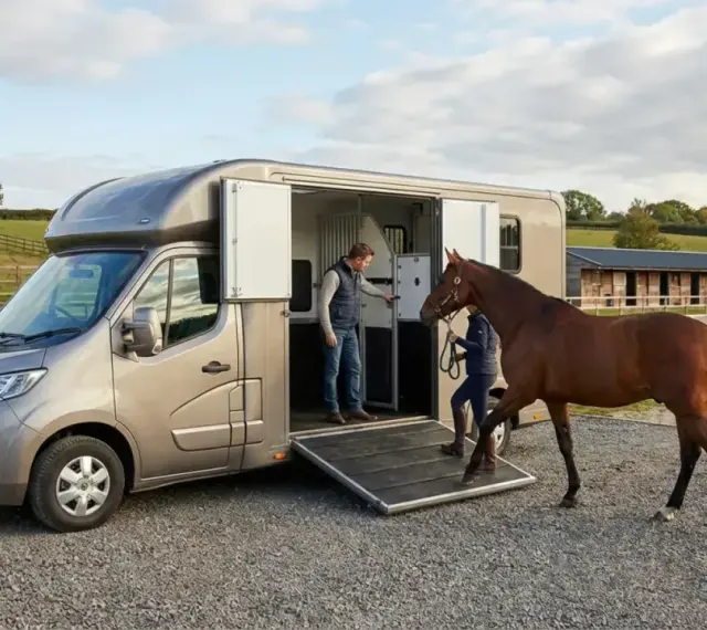 Un homme et une femme chargent un cheval dans un **dimension van chevaux 2 places** sur un terrain d'équitation.