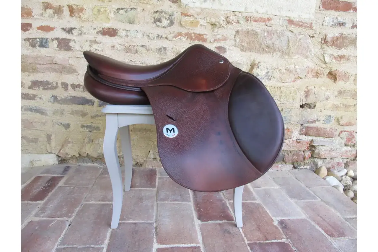 Selle d'équitation en cuir marron, marque Meyer Selle, posée sur un tabouret devant un mur de briques.