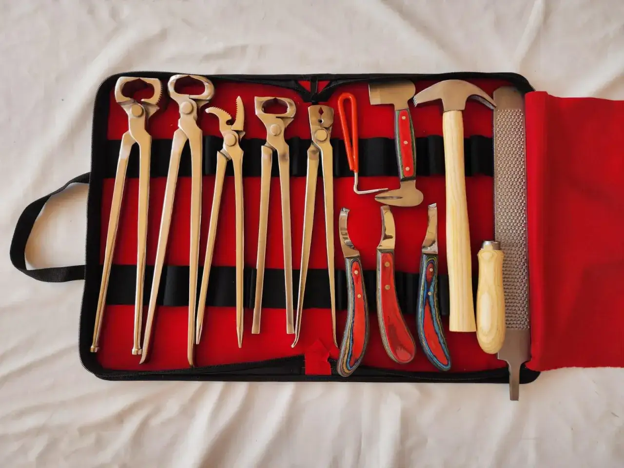 Un étui rouge ouvert révèle un ensemble complet d'outil marechal ferrant : pinces, marteau, râpe et couteaux pour parer les sabots.